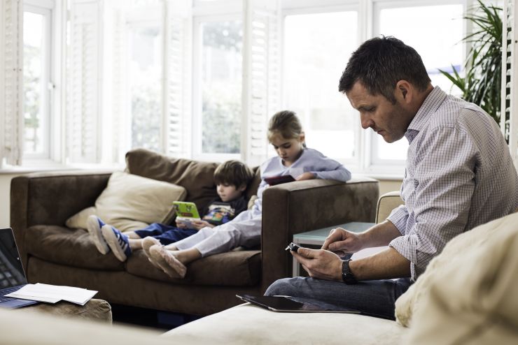 Dad on phone with two children on sofa in background