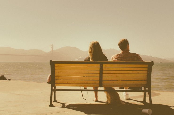 Man, woman and dog on bench looking away from each other