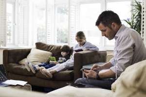 Dad on phone with two children on sofa in background