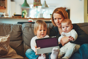 Mum sitting on sofa with two young children looking at ipad